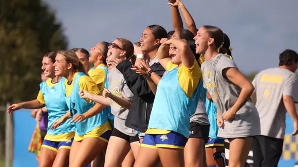 A group of women's soccer players on the bench cheer in celebration