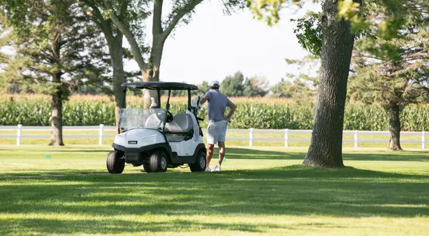 SDSU men's golfer leans on a golf cart on the course.