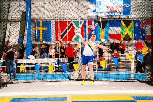 A male track and field thrower releases the weight throw and waits to see his mark
