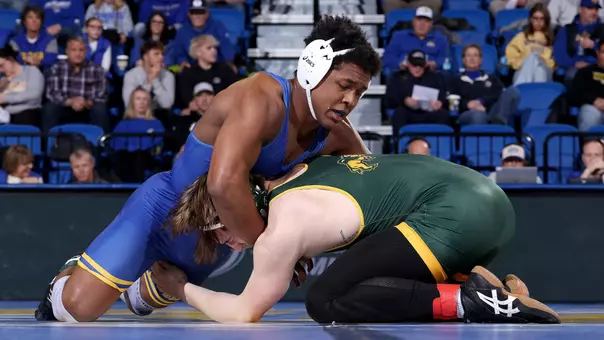 Moses Espinoza-Owens, a wrestler in a blue singlet, holds a headlock on a wrestler in a green singlet during a match