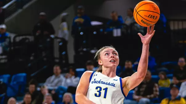 Women's basketball player in a white uniform goes up for a layup during a game