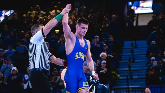 Julian Tagg has his hand raised by a referee after a wrestling match.