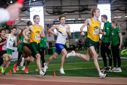 a male runner races around the curve of the track, photographed mid-stride while looking to the side towards the camera