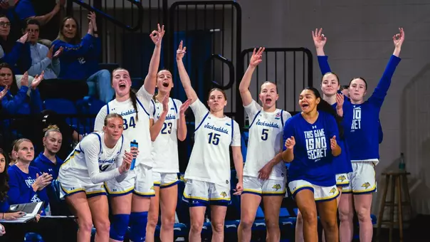 Players on the SDSU bench stand and cheer with their arms raised a game