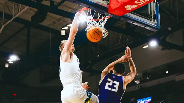 A men's basketball player in a white uniform dunks a basketball