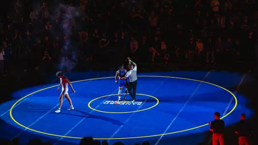 Moses Espinoza-Owens, a wrestler in a blue singlet, has his hand raised by a referee while a wrestler in a white singlet walks off the mat.