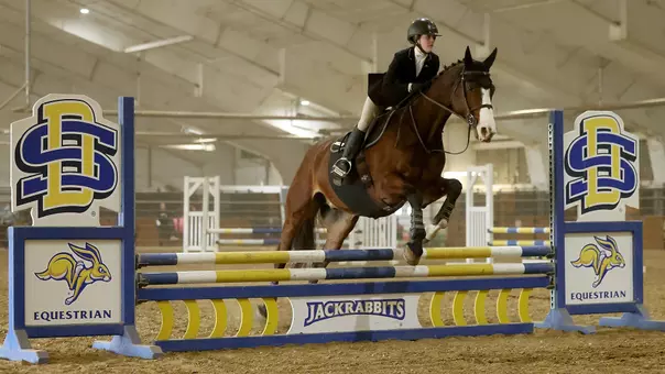 A South Dakota State equestrian rider competes in the jumping seat event of fences as the horse clears a barrier.