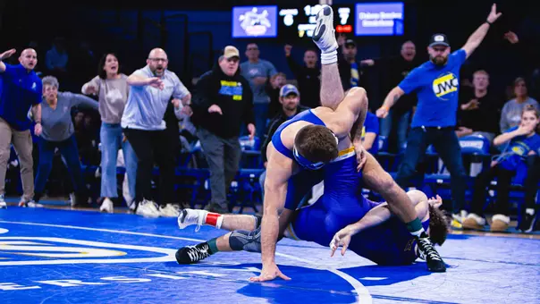 Colin Dupill, a wrestler in a blue singlet, scrambles against a wrestler in a purple singlet during a match with UNI