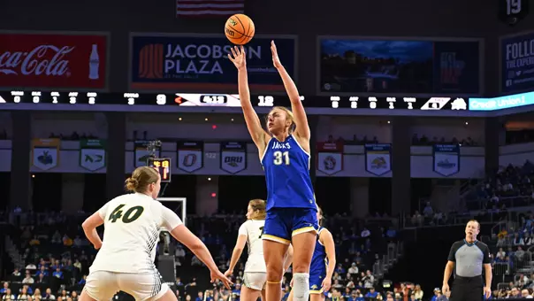 A women's basketball player in a blue uniform goes up for a mid-range shot as a player in white defends