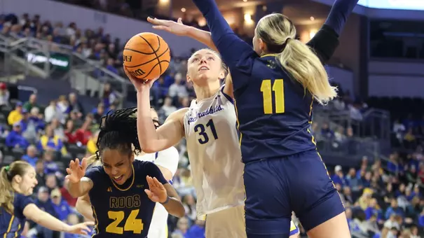 A women's basketball player in a white uniform goes up for a layup as a player in a navy uniform defends