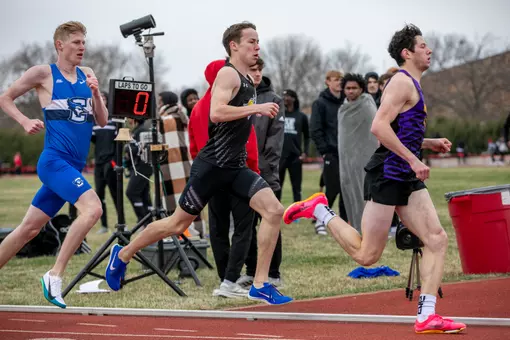 A male runner is depicted from the side running on the straight part of the track between two competitors