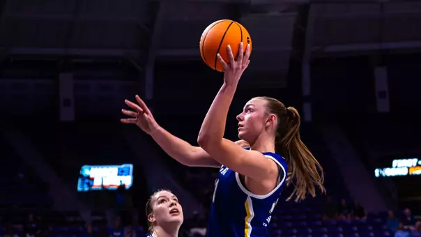 A women's basketball player looks to the basket and extends her arm overhead to shoot during a game