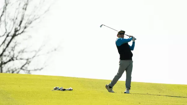 A men's golfer follows through on a swing during competition on a golf course