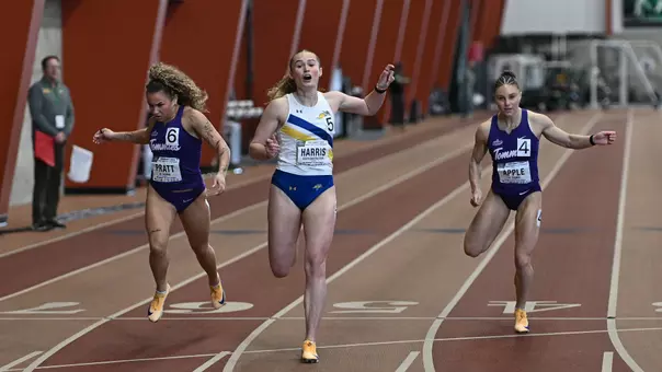A female competitior in a white jersey with blue bottoms crosses the finish line in a track competition