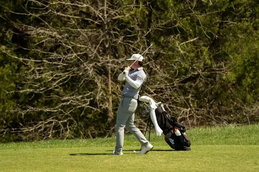 A men's golfer in a white hat follows through with his golf club on the course.