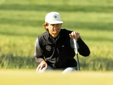 A men's golfer holds his club while reading the green before putting.