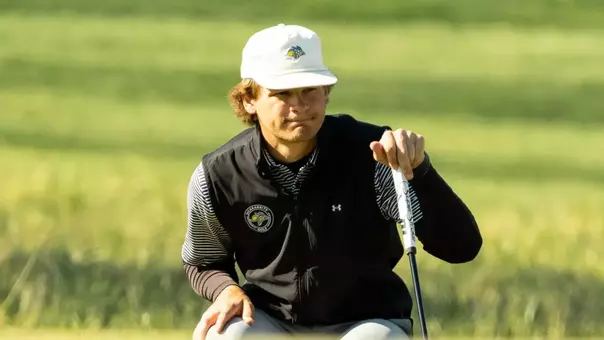 A men's golfer holds his club while reading the green before putting.