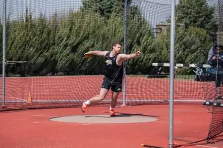A male track athlete in a black uniform spins in the throwers pit with a discus in his hand.