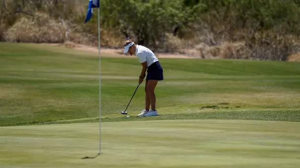 A women's golfer in a white polo and black shirt putts toward the flag during Summit League competition