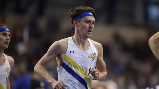 A men's track athlete in a white competition and blue headband runs during competition