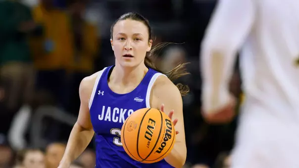 A women's basketball player in a blue uniform dribbles up the court in live action