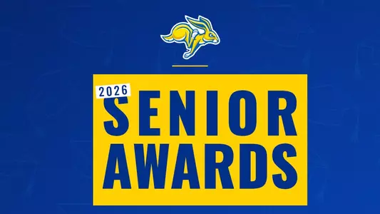 Graphic promoting “2026 Senior Awards.” The design features a blue background with a subtle repeating graduation cap pattern. At the top center is a yellow and blue jackrabbit logo. Below, a large yellow rectangle contains bold blue text reading “2026 SENIOR AWARDS,” with “2026” displayed in a smaller white label at the upper left of the rectangle.