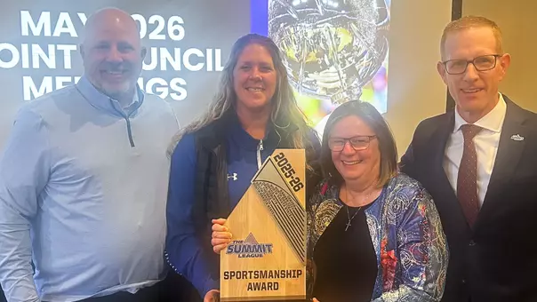 Four people pose for a photo with a Summit League trophy. The trophy is titled Sportsmanship Award and is marked with a Summit League logo. The Summit League schools are listed on the trophy.