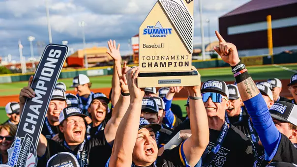 South Dakota State's Luke Luskey hoists the championship trophy at the 2026 Summit League Baseball Championship while his teammates celebrate winning the league tournament around him.