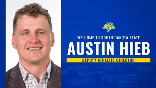 Graphic announcing the hiring of Austin Hieb as Deputy Athletic Director at South Dakota State. Graphic features a left-aligned portrait photo of a person on a light background. The right side of the graphic has a blue design with a faded aerial campus view. Large white and yellow text reads “WELCOME TO SOUTH DAKOTA STATE” and “AUSTIN HIEB” with “DEPUTY ATHLETIC DIRECTOR” in a yellow bar beneath the name.