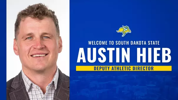 Graphic announcing the hiring of Austin Hieb as Deputy Athletic Director at South Dakota State. Graphic features a left-aligned portrait photo of a person on a light background. The right side of the graphic has a blue design with a faded aerial campus view. Large white and yellow text reads “WELCOME TO SOUTH DAKOTA STATE” and “AUSTIN HIEB” with “DEPUTY ATHLETIC DIRECTOR” in a yellow bar beneath the name.