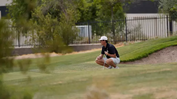 A men's golfer on a course in a crouched stance analyzing a shot