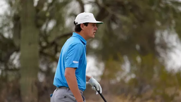 A men's golfer in a light blue polo walks to the tee during a round