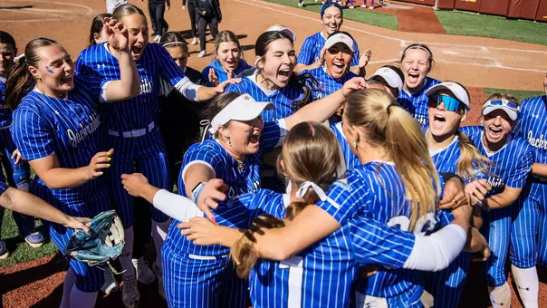 A group of women in blue jerseys jump up and celebrate in a huddle