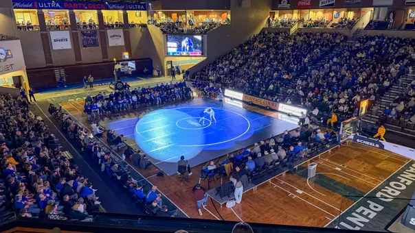Two wrestlers grapple on a blue mat in front of several fans at the Sanford Pentagon.
