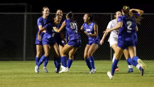 A group of women in blue soccer uniforms race to each other in celebration