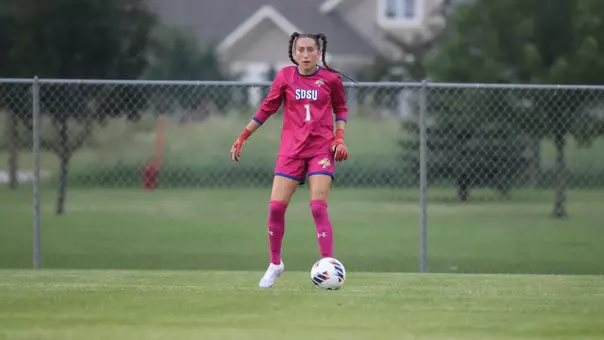 a woman in a pink soccer uniform looks ahead while a soccer ball sits at her feet