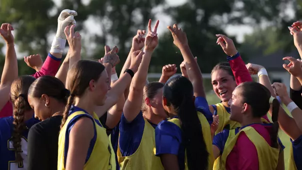 A group of women huddle up with their arms raised as they prepare to play a soccer game