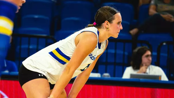 A volleyball in white stands ready with her hands on her knees, waiting for a serve to come in.