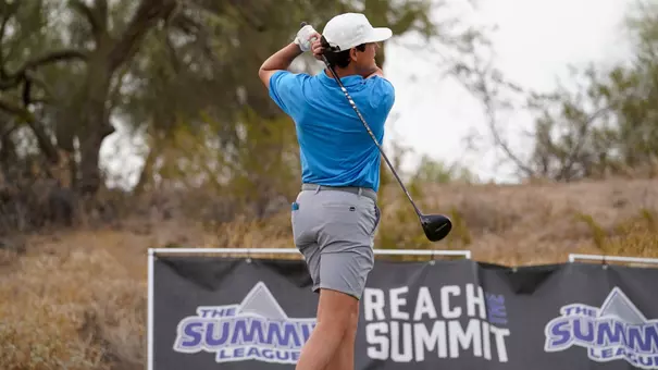 Golfer follows through on a tee shot during a golf tournament, with Summit League championship signage visible in the background.