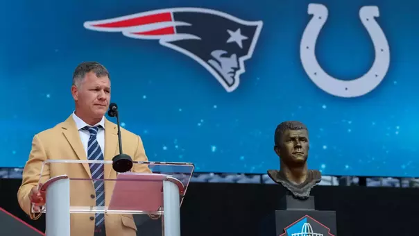 Adam Vinatieri stands at the podium and is flanked by his Pro Football Hall of Fame bust during enshrinement ceremonies Aug. 8, 2026, at Tom Benson Stadium in Canton, Ohio.