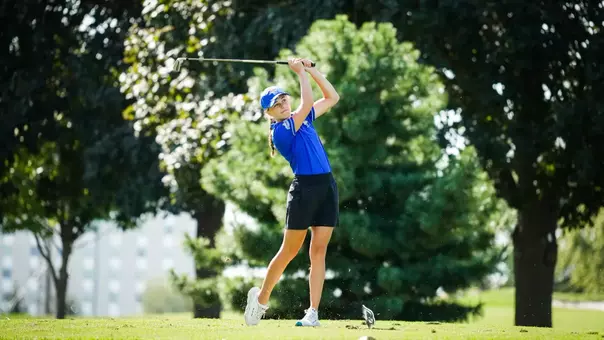 A golfer in blue swings a club.