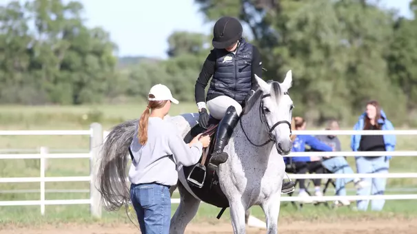 A coach helps an athlete that is sitting on horse in equestrian arena outdoors