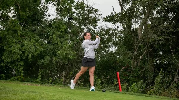A golfer in a white hoodie hits a golf ball with an iron.