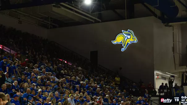 Fans watch a volleyball as a Jackrabbit sign hangs above them.