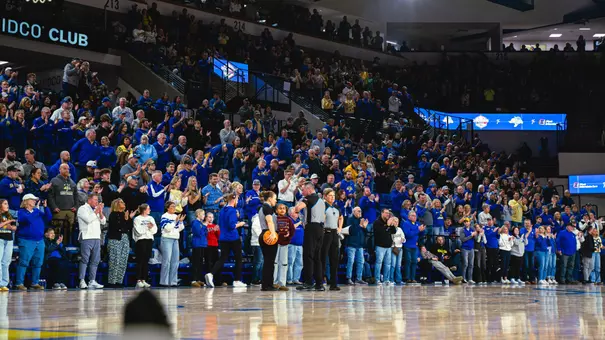 A crowd in a basketball arena stands and cheers during a break in on-court action
