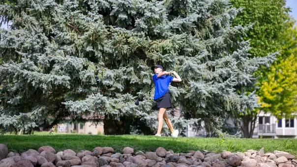 A South Dakota State golfer follows through on a tee shot during a tournament round, with trees in the background.