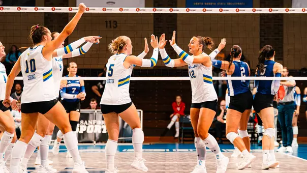 Two volleyball players in white uniforms high five after a point.