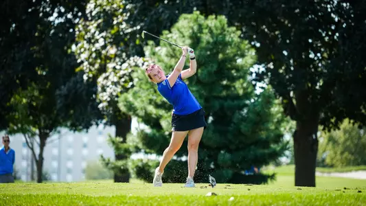 A golfer in a blue polo swing a golf club.