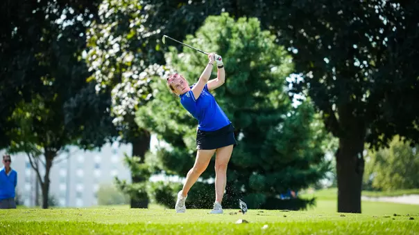 A golfer in a blue polo swing a golf club.