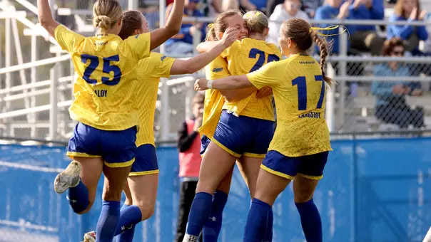 Womens soccer players in yellow uniforms with blue shorts race to each other following a goal to celebrate